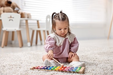 Photo of Cute little girl playing with toy xylophone on floor at home