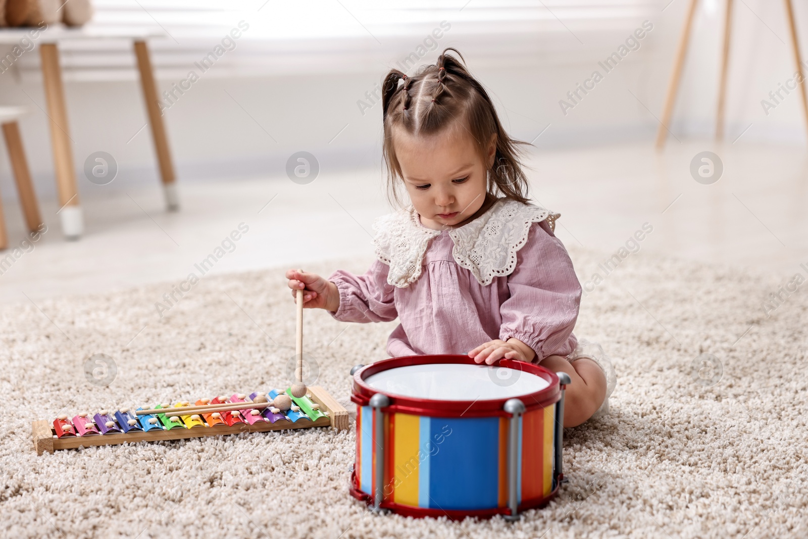 Photo of Cute little girl playing with toy drum and drumstick on floor at home