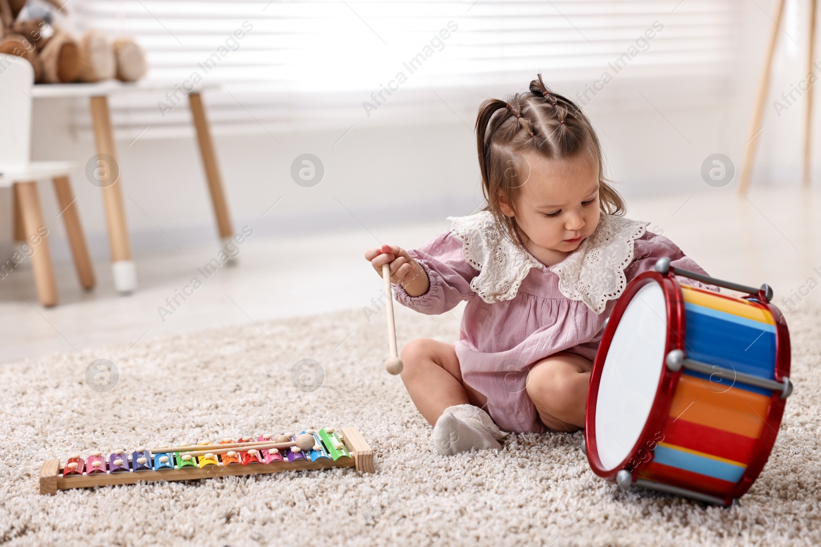 Photo of Cute little girl playing with toy drum and drumstick at home, space for text