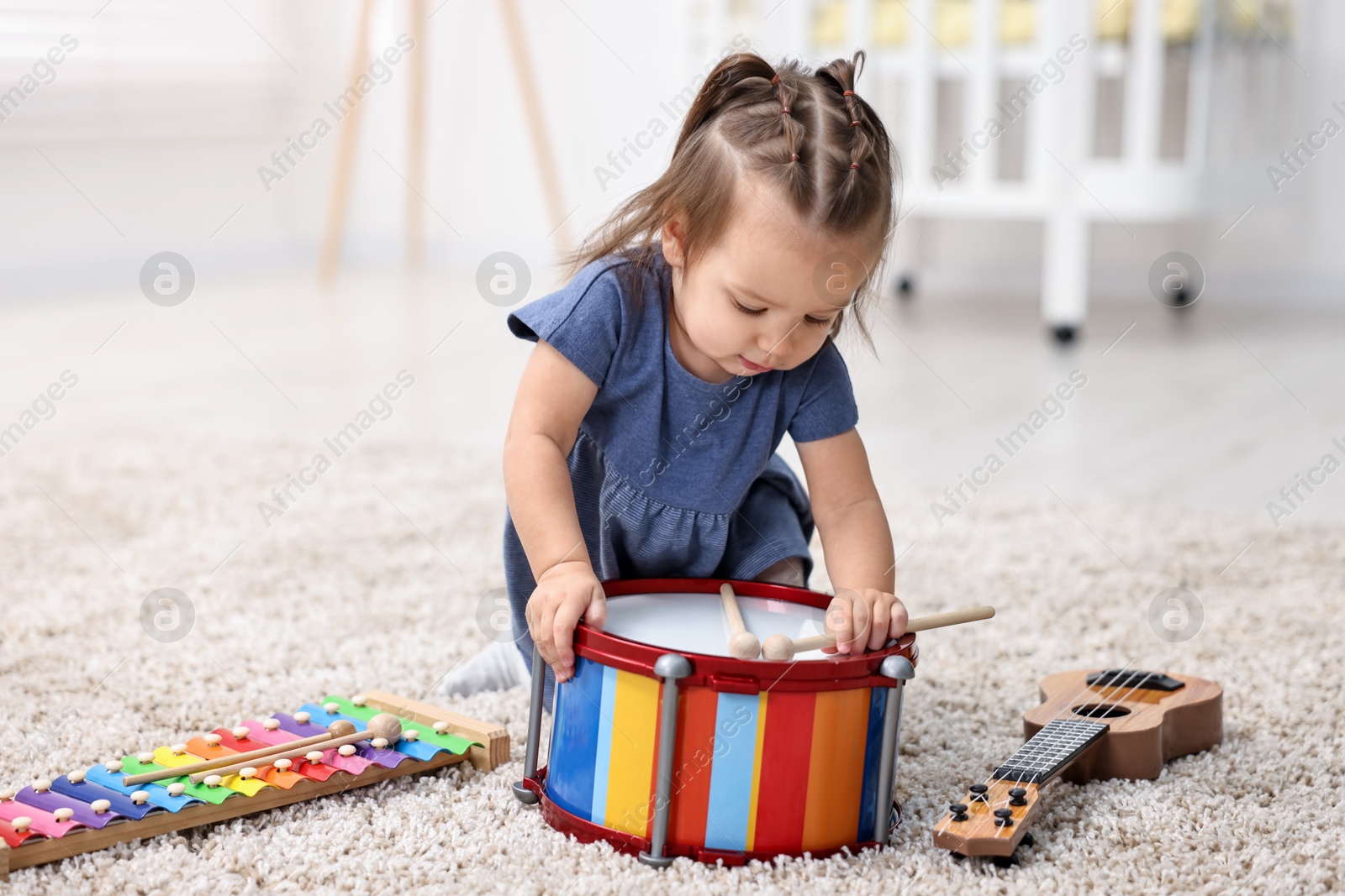 Photo of Cute little girl playing with toy drum and drumsticks on floor at home