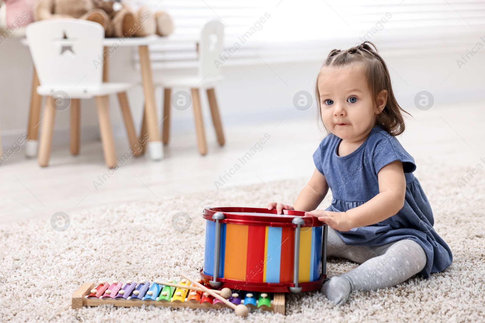 Photo of Cute little girl playing with toy drum on floor at home, space for text