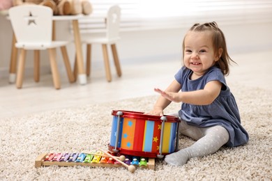 Photo of Cute little girl playing with toy drum on floor at home, space for text