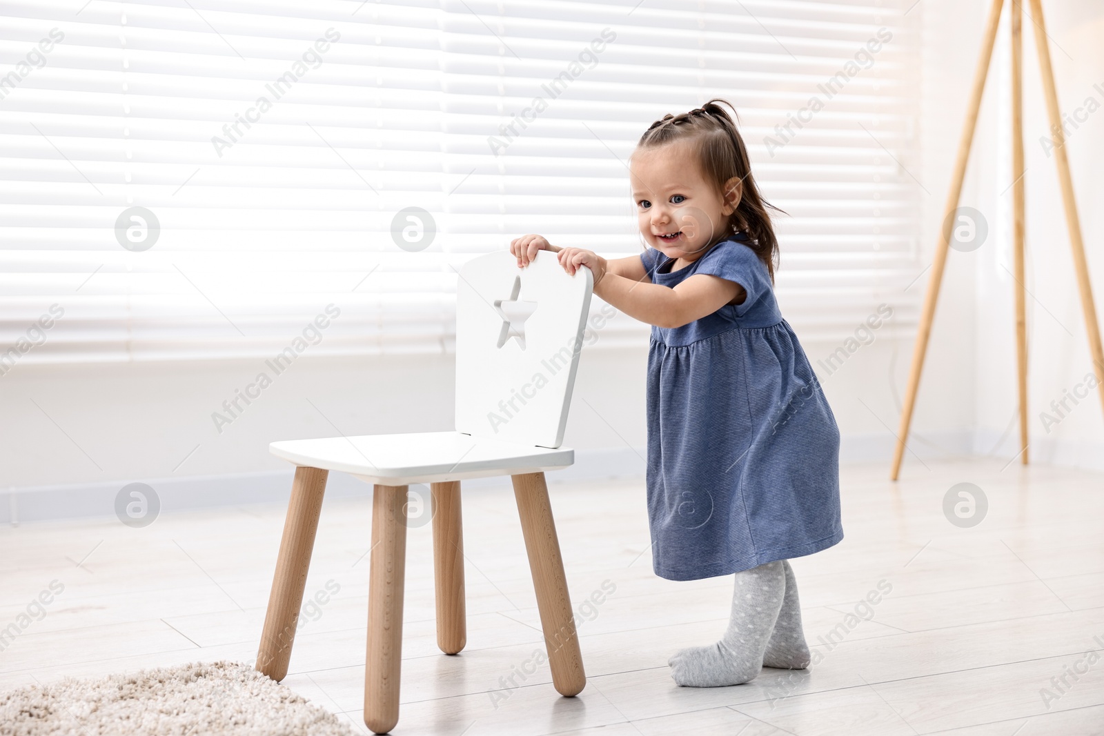 Photo of First steps. Cute little baby with small chair at home