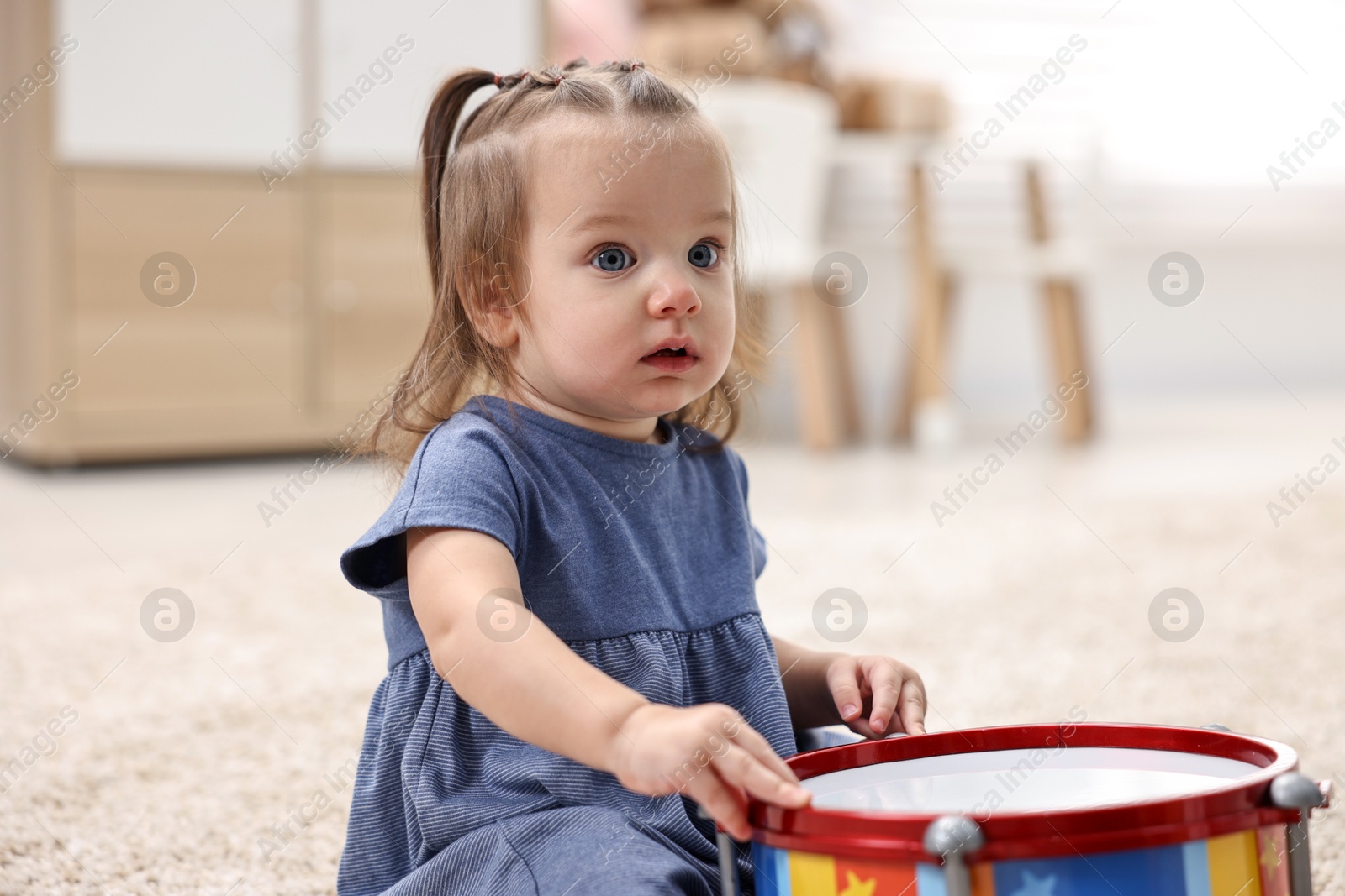 Photo of Cute little girl playing with toy drum on floor at home