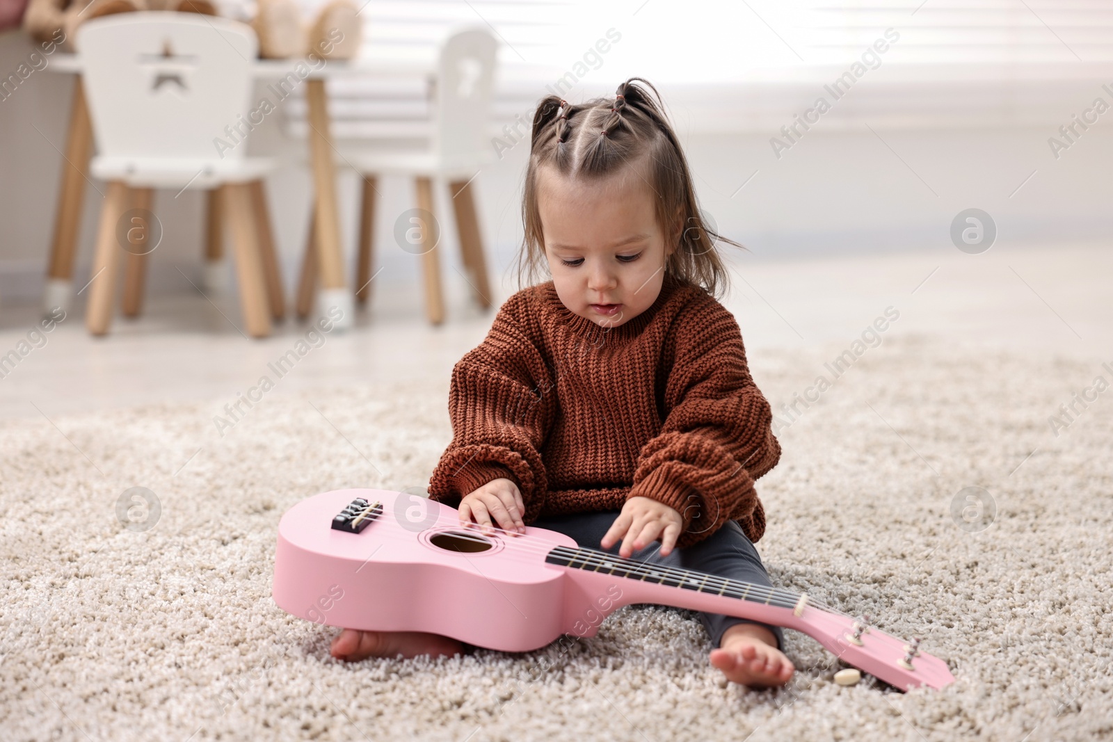 Photo of Cute little girl playing with toy guitar on floor at home