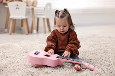 Photo of Cute little girl playing with toy guitar on floor at home