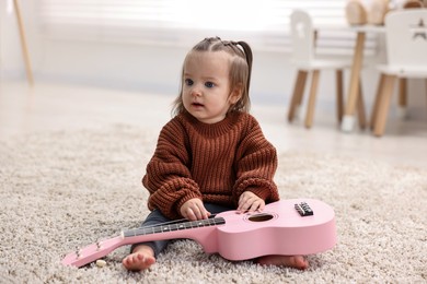 Photo of Cute little girl playing with toy guitar on floor at home