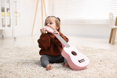 Photo of Cute little girl playing with toy guitar on floor at home