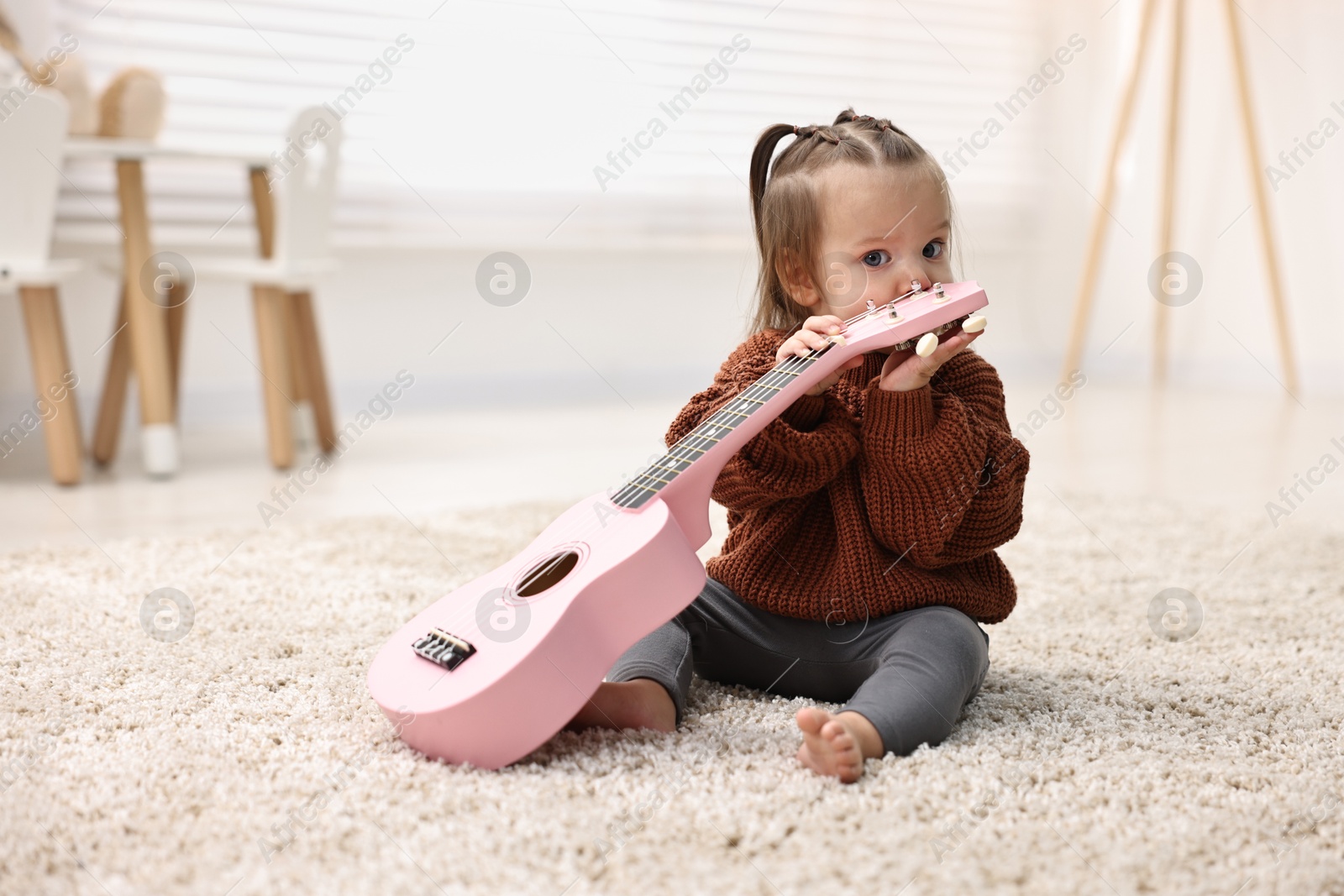 Photo of Cute little girl playing with toy guitar on floor at home