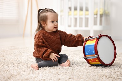 Photo of Cute little girl playing with toy drum on floor at home