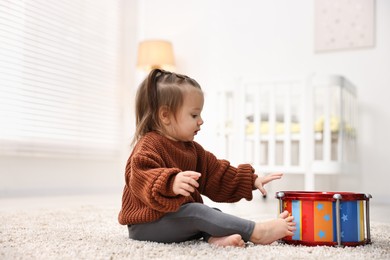 Photo of Cute little girl playing with toy drum on floor at home