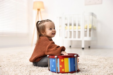 Photo of Cute little girl playing with toy drum on floor at home