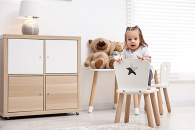 Photo of First steps. Cute little baby on small chair at home