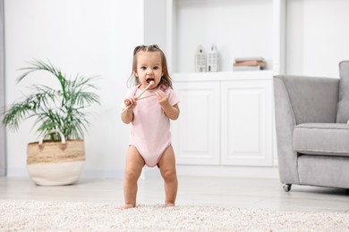 Photo of First steps. Cute little baby with drumsticks learning to walk at home