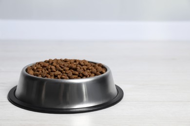 Photo of Dry pet food granules in feeding bowl on floor indoors, space for text