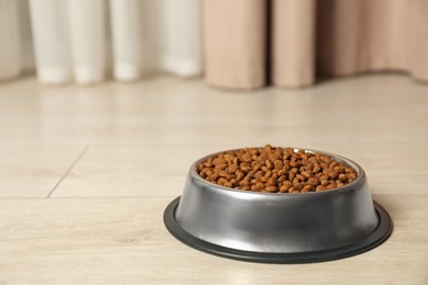 Photo of Dry pet food granules in feeding bowl on floor indoors, space for text