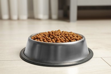 Photo of Dry pet food granules in feeding bowl on floor indoors