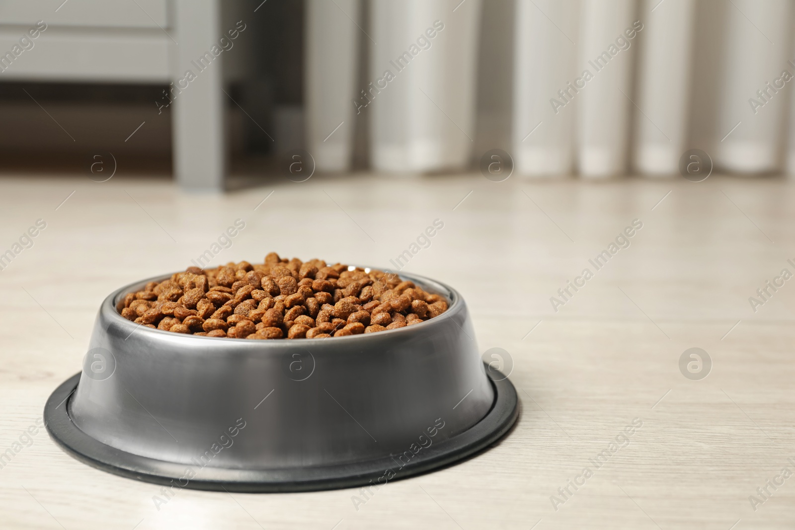 Photo of Dry pet food granules in feeding bowl on floor indoors, space for text