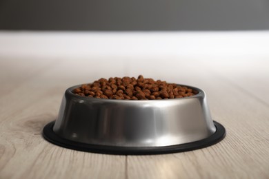 Photo of Dry pet food granules in feeding bowl on floor indoors