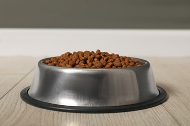 Photo of Dry pet food granules in feeding bowl on floor indoors