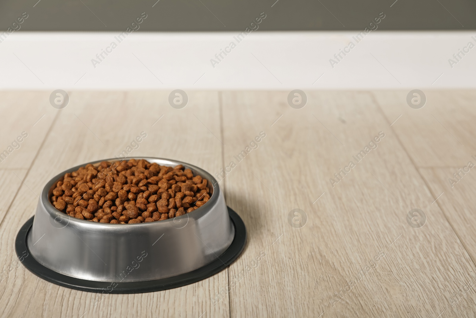 Photo of Dry pet food granules in feeding bowl on floor indoors, space for text