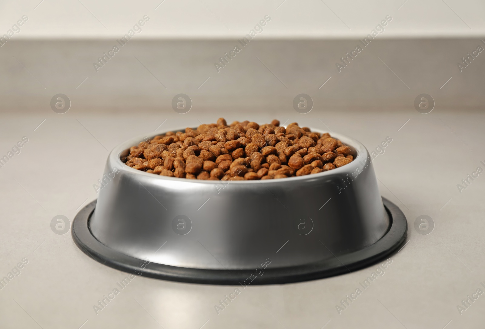 Photo of Dry pet food granules in feeding bowl on floor indoors