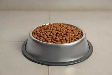 Photo of Dry pet food granules in feeding bowl on floor