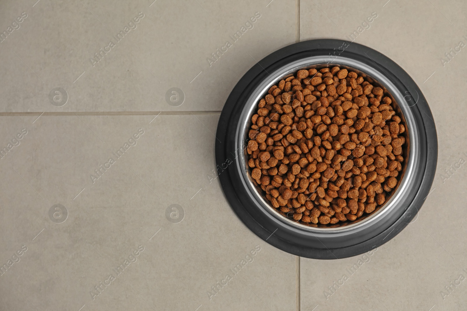 Photo of Dry pet food granules in feeding bowl on floor, top view. Space for text