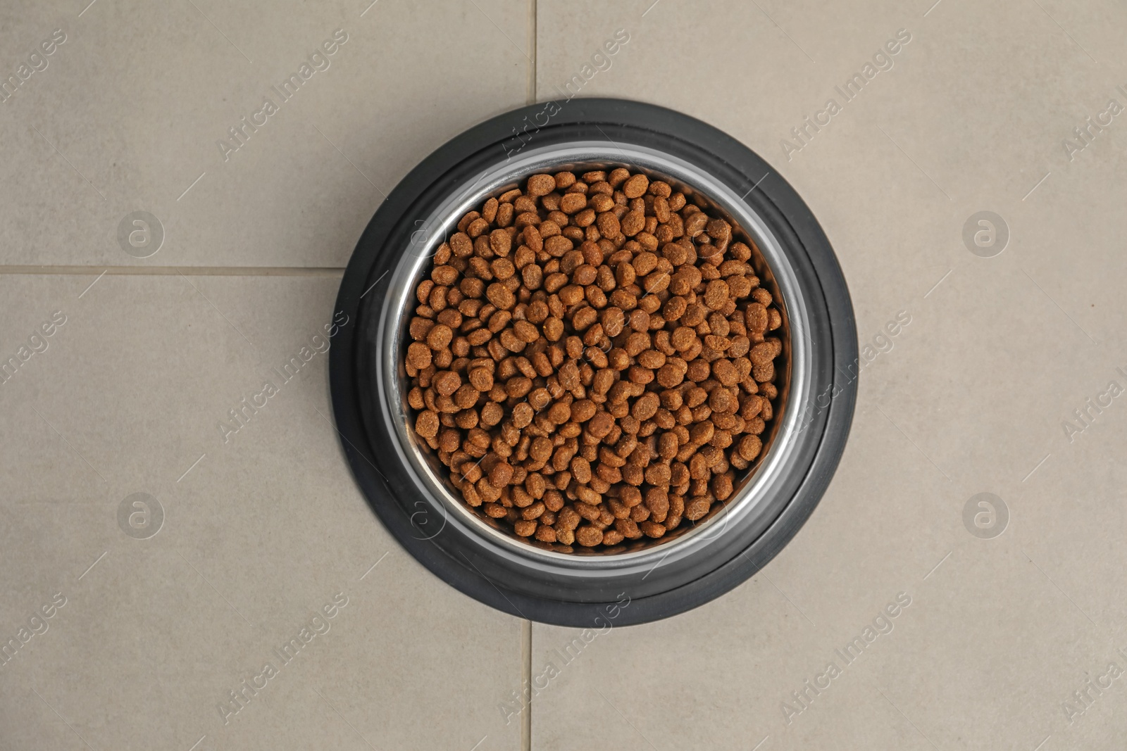 Photo of Dry pet food granules in feeding bowl on floor, top view