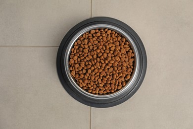 Photo of Dry pet food granules in feeding bowl on floor, top view