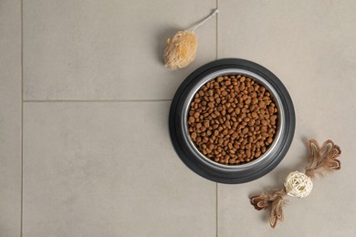 Photo of Dry pet food granules in feeding bowl and cat toys on floor, flat lay. Space for text