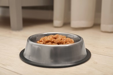 Photo of Wet pet food in feeding bowl on floor indoors