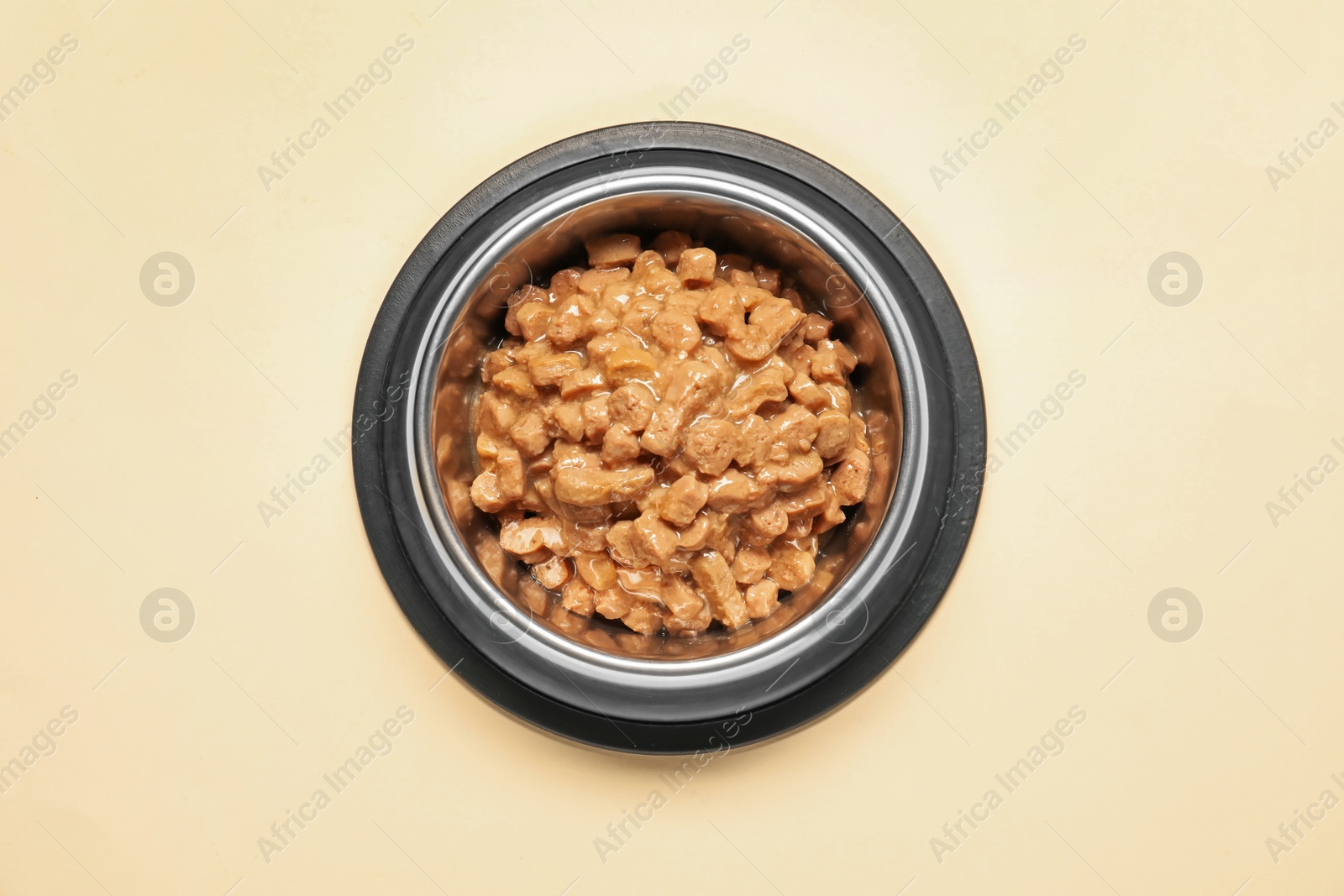 Photo of Wet pet food in feeding bowl on pale yellow background, top view