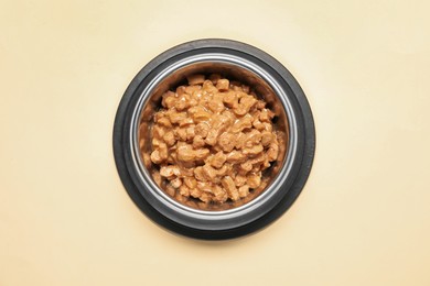 Photo of Wet pet food in feeding bowl on pale yellow background, top view