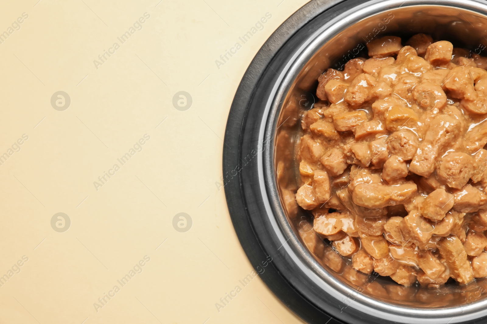 Photo of Wet pet food in feeding bowl on pale yellow background, top view. Space for text