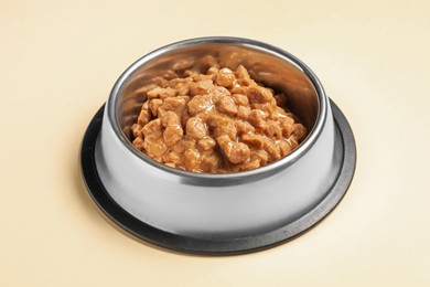 Photo of Wet pet food in feeding bowl on pale yellow background