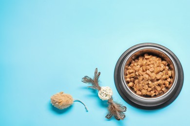 Photo of Wet pet food in feeding bowl and cat toys on light blue background, flat lay. Space for text