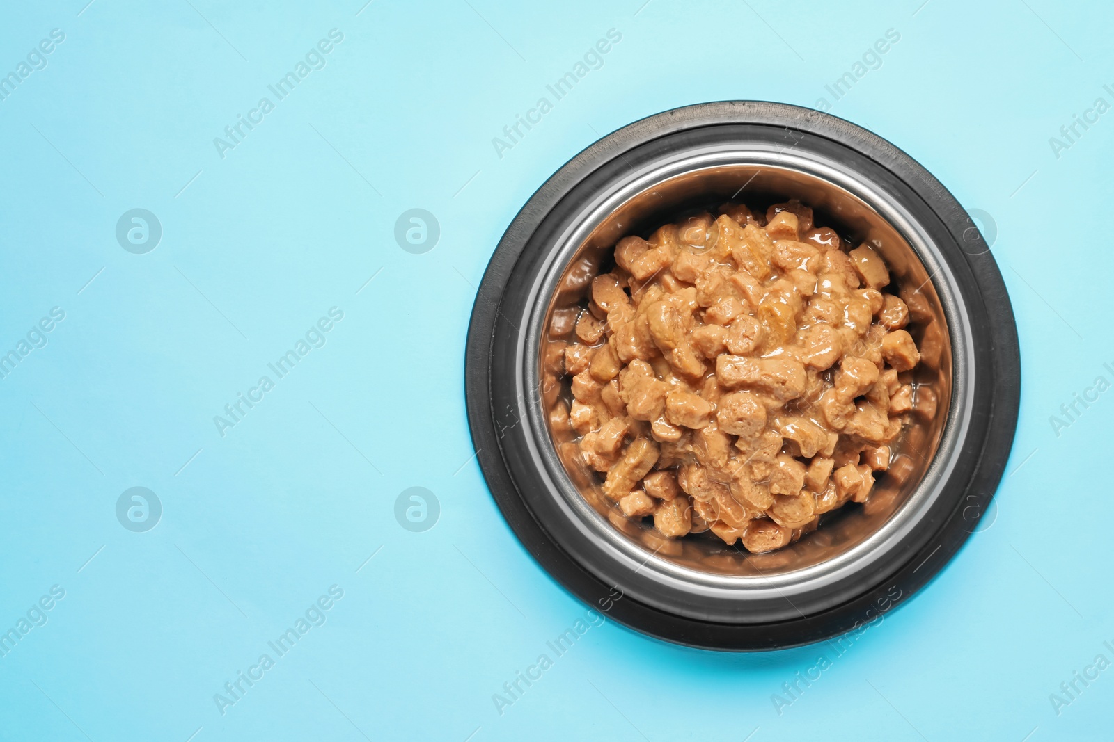 Photo of Wet pet food in feeding bowl on light blue background, top view Space for text