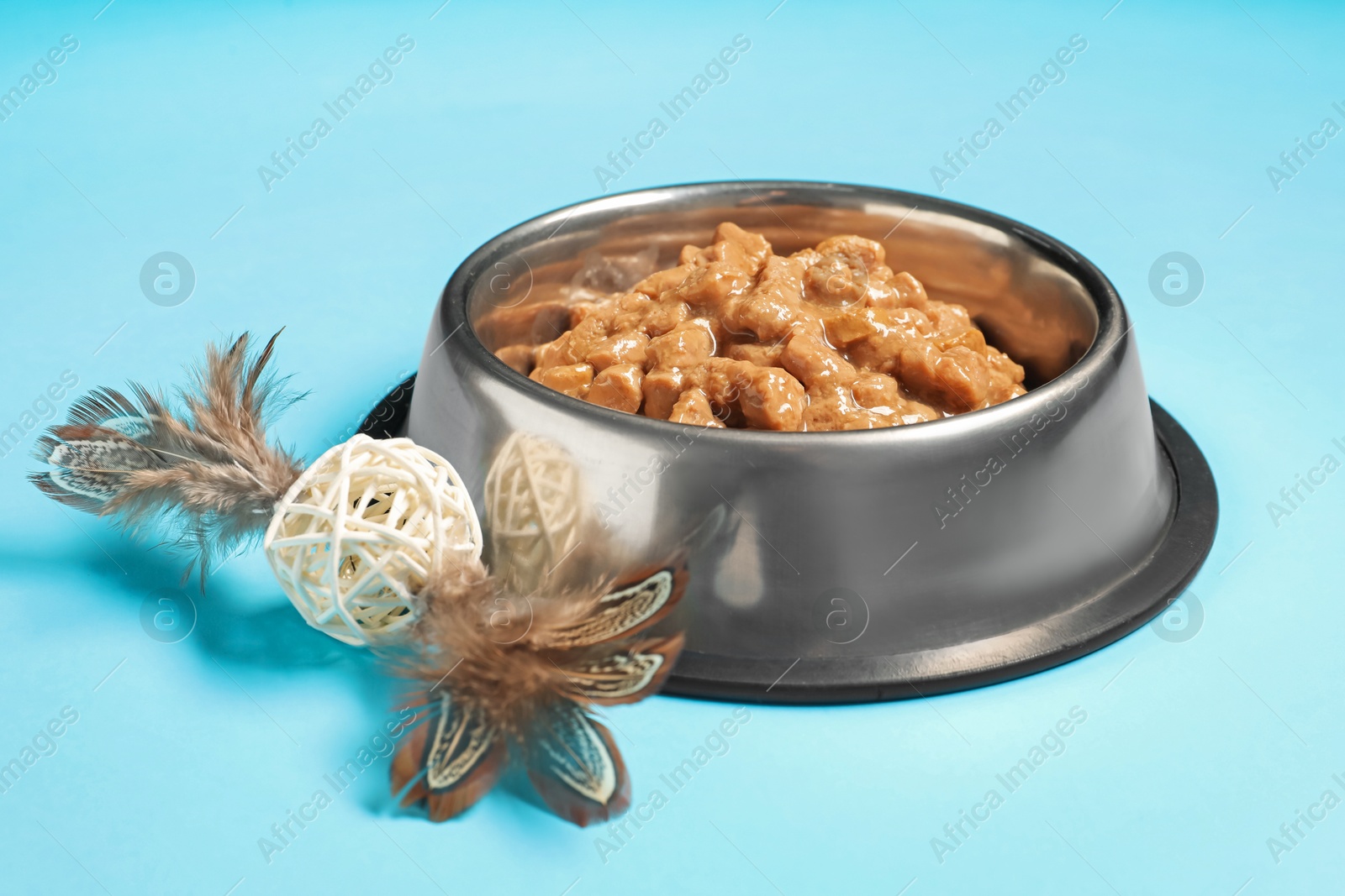 Photo of Wet pet food in feeding bowl and cat toy on light blue background