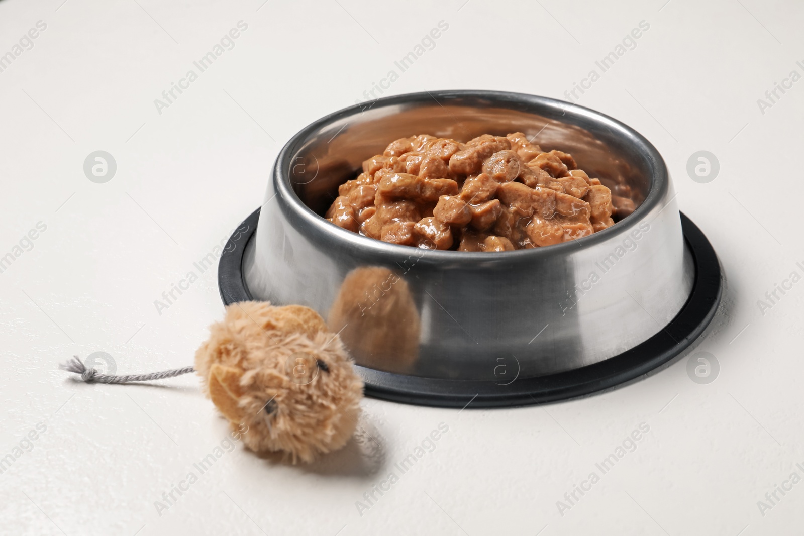 Photo of Wet pet food in feeding bowl and cat toy on white background