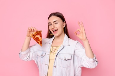 Woman with pizza winking and showing OK gesture on pink background