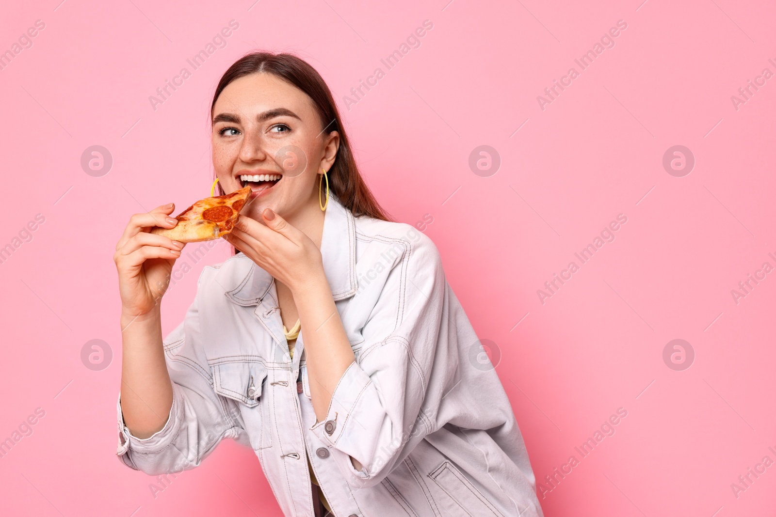 Photo of Beautiful woman eating pizza on pink background, space for text