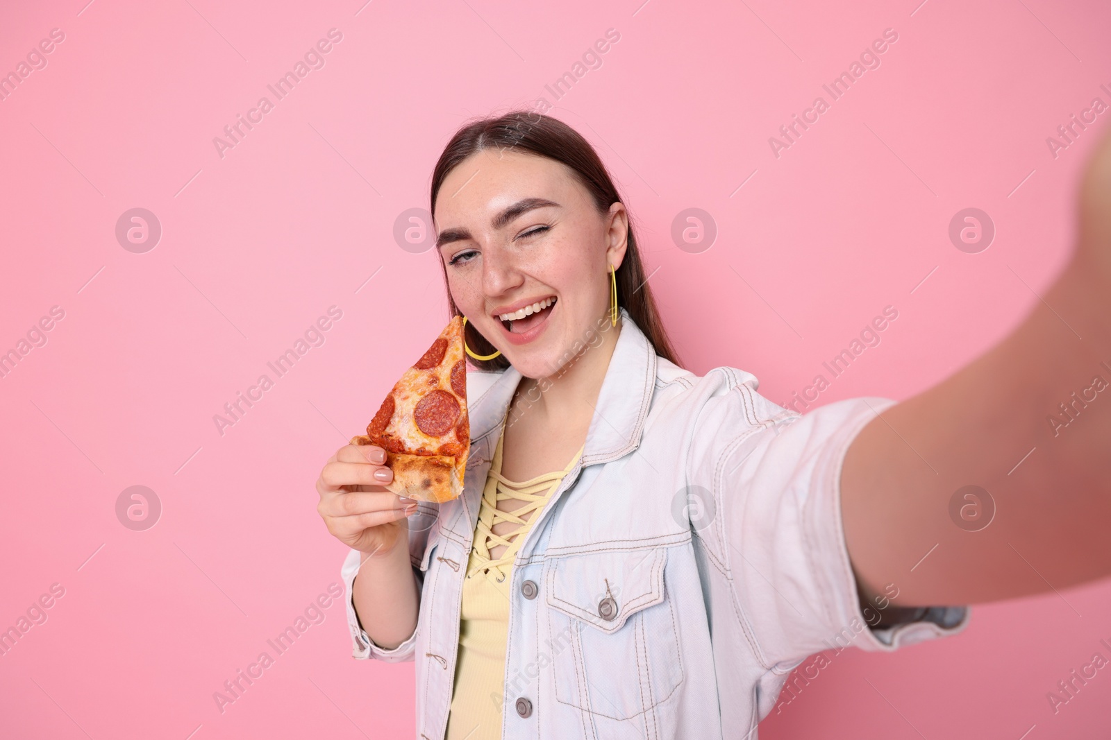 Photo of Beautiful woman with delicious pizza taking selfie on pink background, space for text