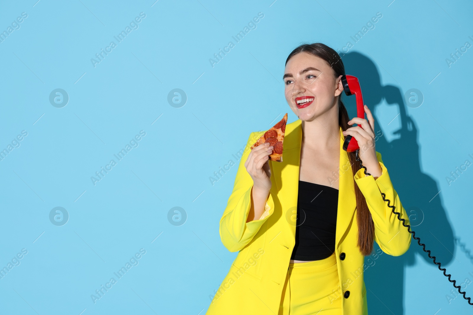 Photo of Beautiful woman with delicious pizza and telephone on light blue background, space for text