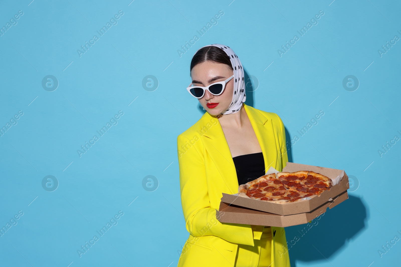 Photo of Stylish woman with delicious pizza on light blue background, space for text