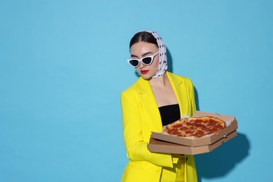 Photo of Stylish woman with delicious pizza on light blue background, space for text