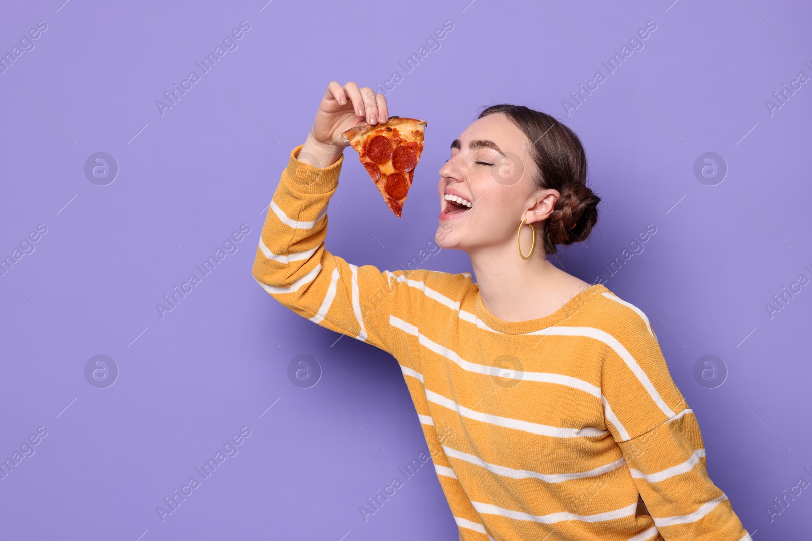 Photo of Beautiful woman with piece of delicious pizza on violet background, space for text