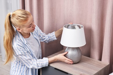 Photo of Female decorator arranging lamp onto nightstand indoors