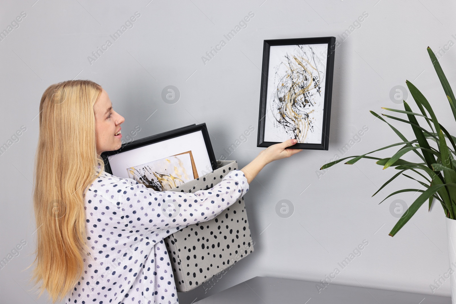 Photo of Smiling decorator hanging abstract picture on wall indoors