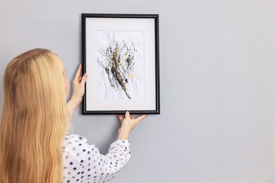 Photo of Female decorator hanging abstract picture indoors, back view. Space for text